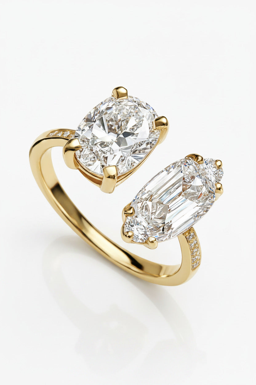 A gold ring with two diamond gemstones, one oval and one marquise-cut, displayed on a white marble surface.