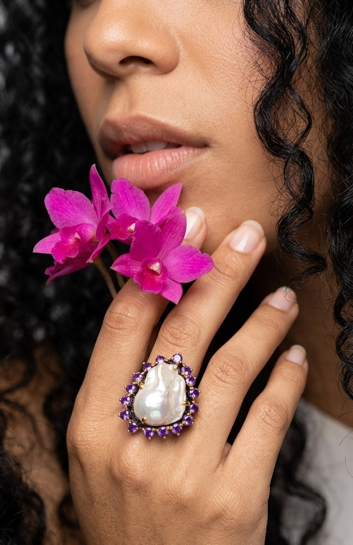 Close-up of a woman's hand holding pink flowers with a detailed ring on her finger.