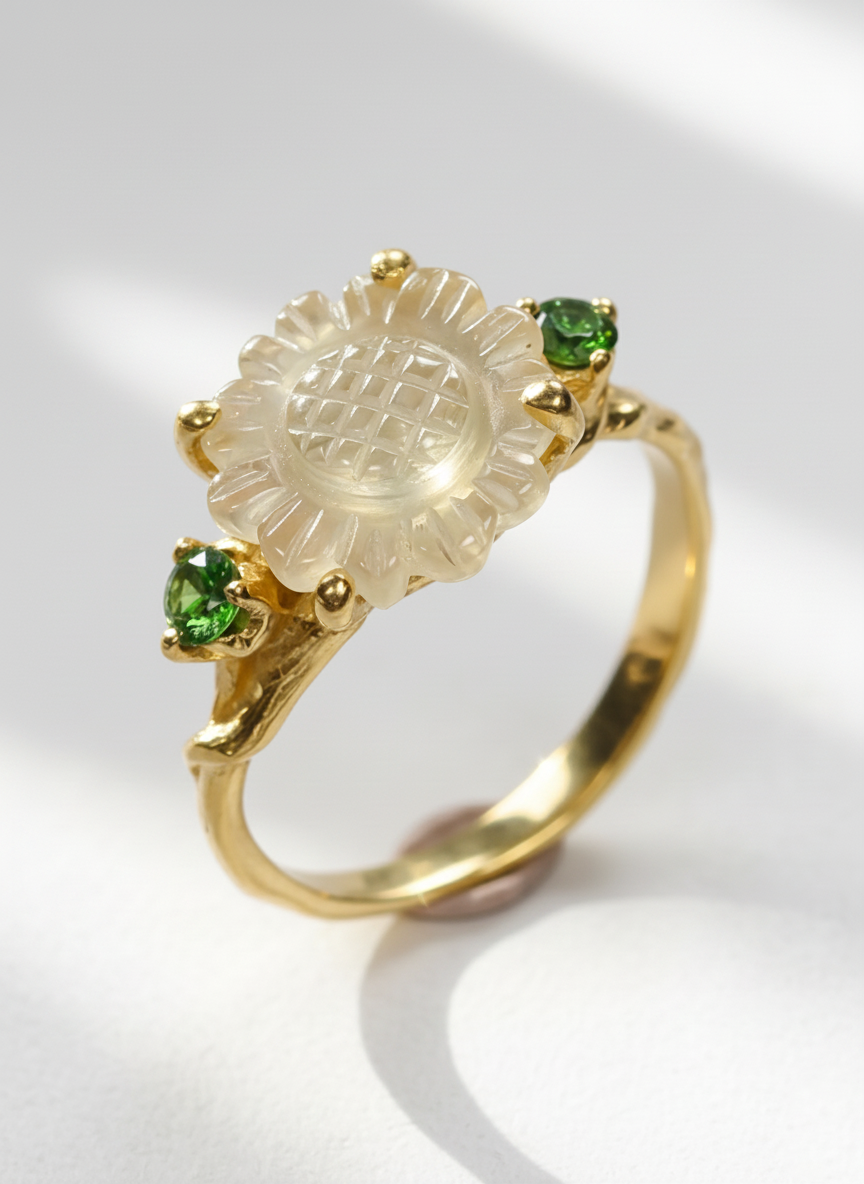 Gold ring with a carved flower stone and green gemstones on a white background