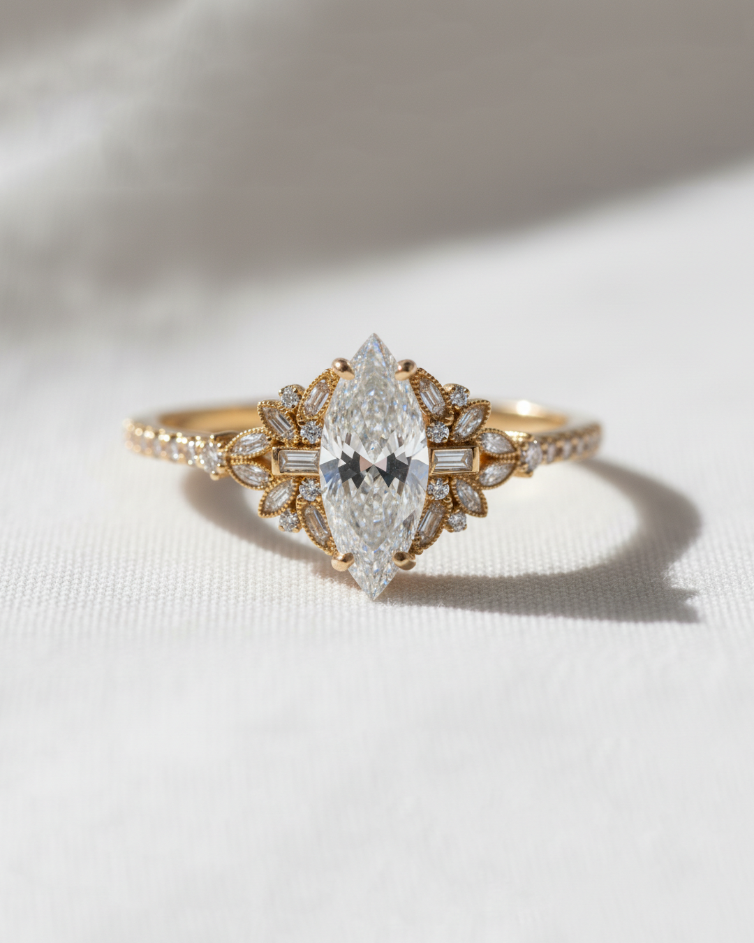 A gold ring featuring a marquise-cut diamond center stone and smaller diamonds, photographed on a textured white fabric background with soft shadows.