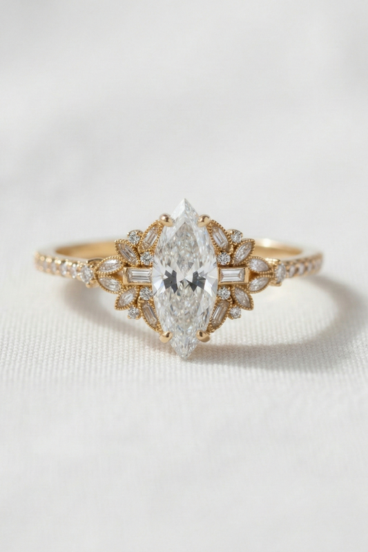 A yellow gold ring featuring a marquise-cut diamond center stone and smaller diamonds along the shoulders, set against a soft white textured background.