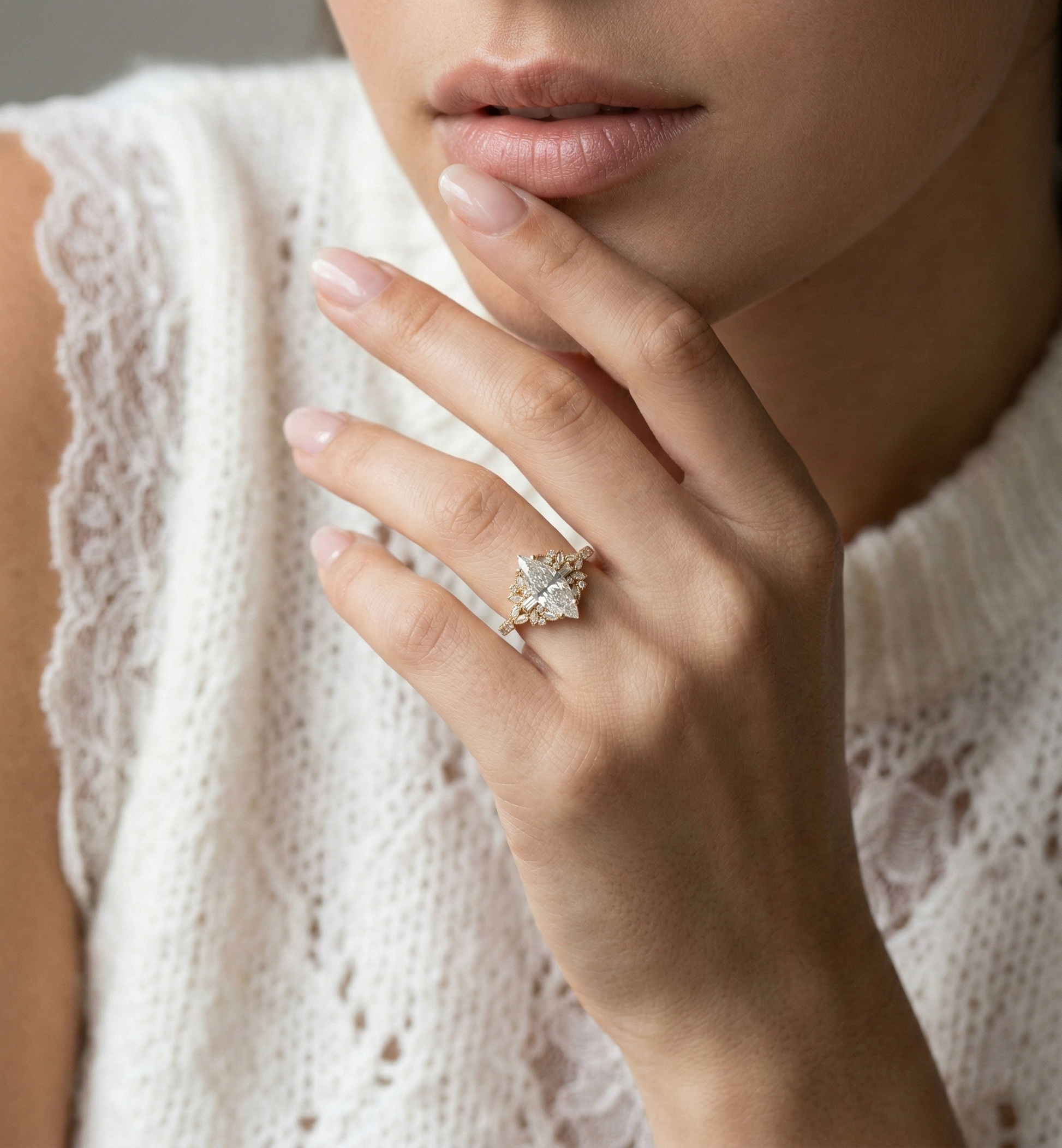 A close-up lifestyle shot of a woman wearing a delicate gold ring with a clear, starburst-shaped gemstone on her finger, set against a soft-focus background of her white lace-trimmed top.