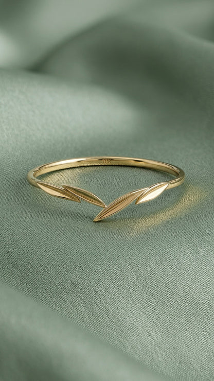 A delicate gold ring with a leaf design, resting on a soft, draped sage green fabric background.